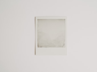 A blank Polaroid photograph is positioned against a plain white background. The image inside the photograph is not developed or visible, resulting in an empty, grey-ish square within the white frame.