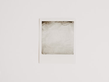 A blank Polaroid-style photograph with a white border lies flat against a light, neutral background. The photo area is empty, showing only a washed-out pale gray color.