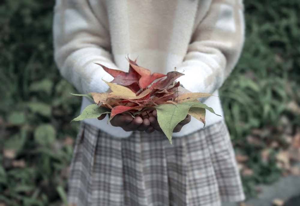 woman in white long sleeve shirt holding red and green leaves