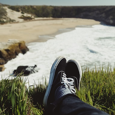 person in blue denim jeans and black and white sneakers sitting on green grass near body