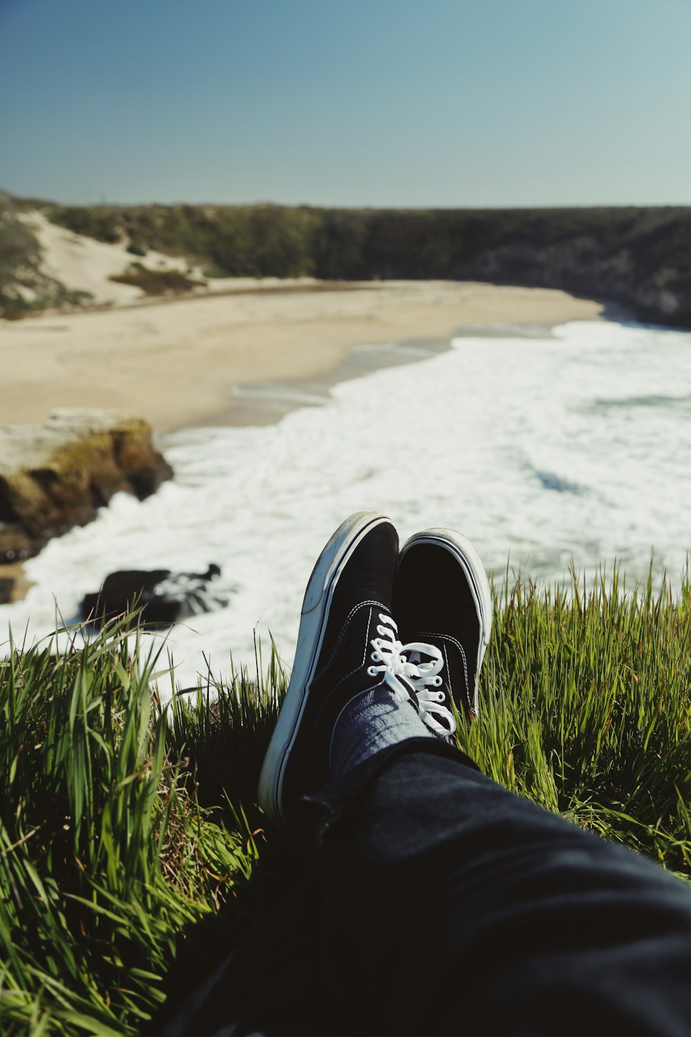 person in blue denim jeans and black and white sneakers sitting on green grass near body