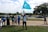 A group of people is gathered on a lawn with the United States Capitol building in the background. One person is holding a blue flag with a white crescent and star. Another person is holding a sign with a message about family and China. The scene appears to be a protest or demonstration.
