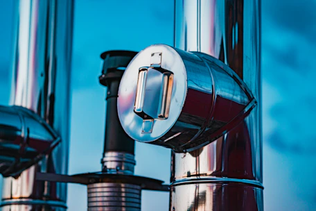 Close-up of industrial pipelines with safety valves reflecting sunlight at an oil refinery.