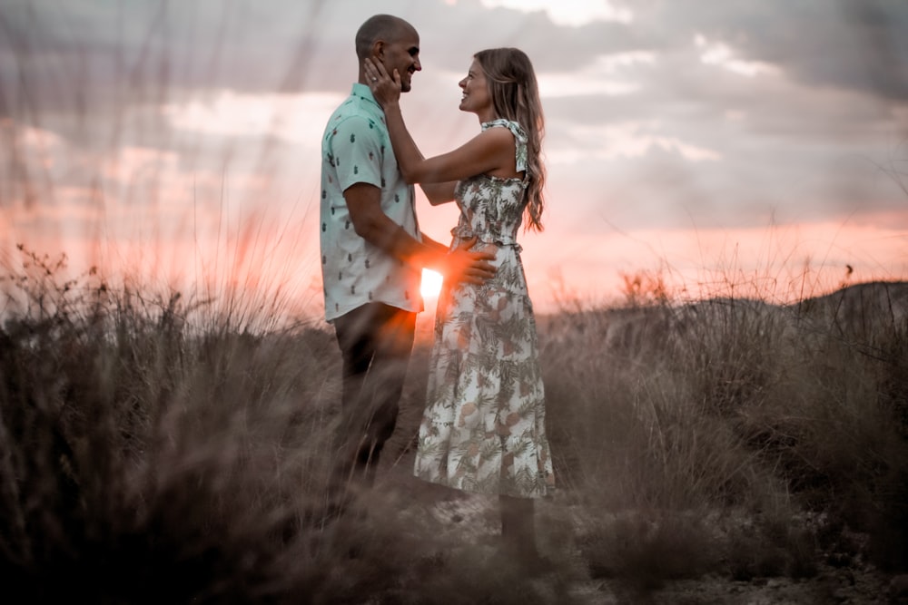 man and woman kissing on grass field during sunset