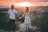 A happy couple smiling and holding hands in a park during sunset.