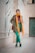 A stylish individual wearing a colorful, artsy outfit, standing confidently in an urban setting.