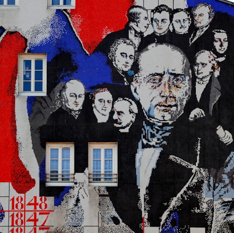 A large mural is painted on a building wall featuring historical figures dressed in 19th-century attire. The faces are depicted in a collage style with a mix of colors, primarily red, blue, black, and white. Two rectangular windows are integrated into the artwork. The mural seems to be divided into panels, with numbers like 1848 and 1847 painted at the bottom left corner.