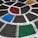 A painted section of pavement features a geometric design composed of white lines forming a segmented circular pattern. The segments are filled with different bright colors, including red, blue, green, and yellow, set against a dark asphalt background.