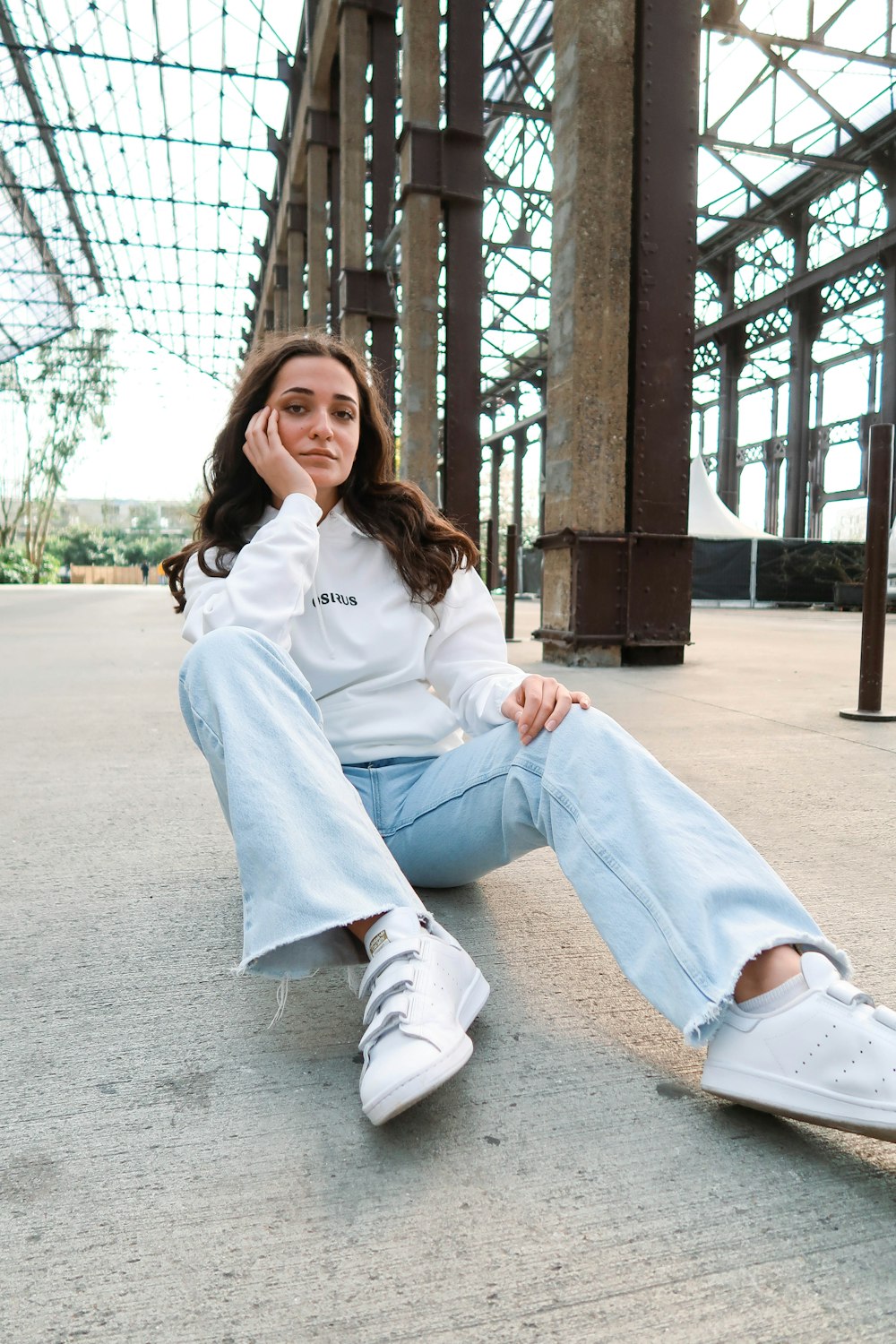 woman in white long sleeve shirt and blue denim jeans sitting on gray concrete floor