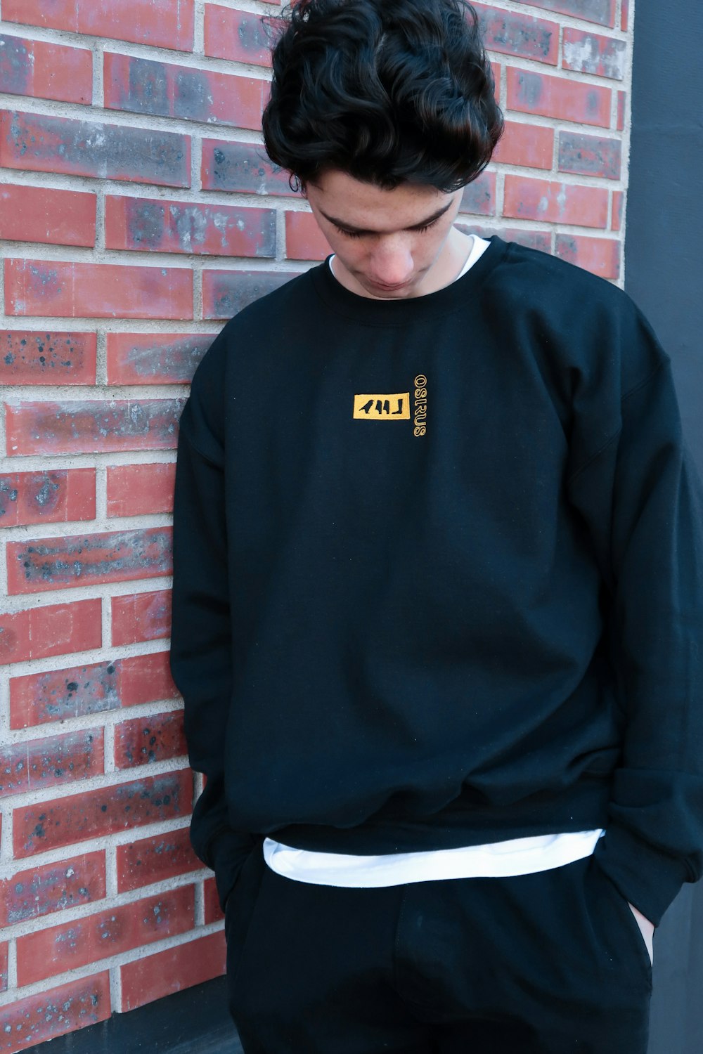 man in blue crew neck sweater standing beside brown brick wall