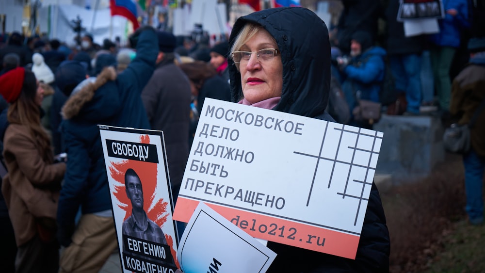 woman in black jacket holding white and red poster