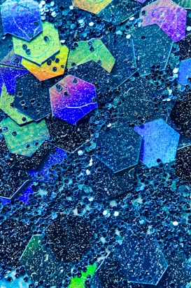 A collection of multicolored hexagonal shapes and dark spherical beads scattered across a surface, creating a vibrant and textured pattern with a shiny, reflective quality.