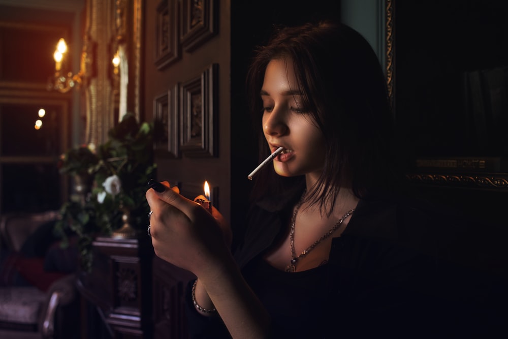 woman lighting cigarette stick in front of green plant