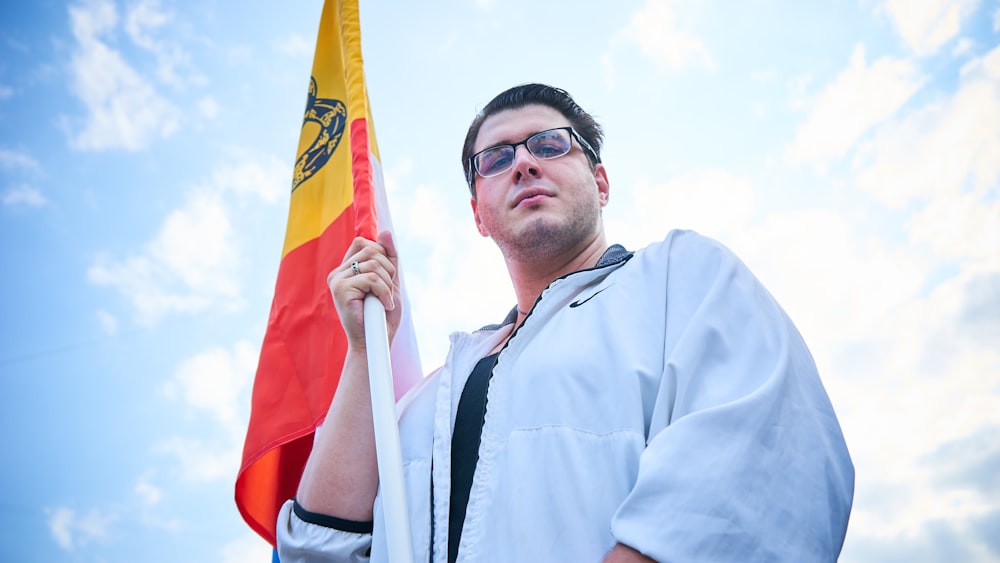 homem em azul botão até camisa vestindo óculos de sol pretos segurando bandeira vermelha e amarela