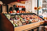 A close-up of fresh, colorful fruits and vegetables neatly arranged on wooden shelves in a cozy local market setting.