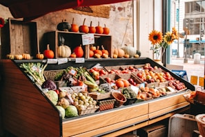 A close-up of fresh, colorful fruits and vegetables neatly arranged on wooden shelves in a cozy local market setting.
