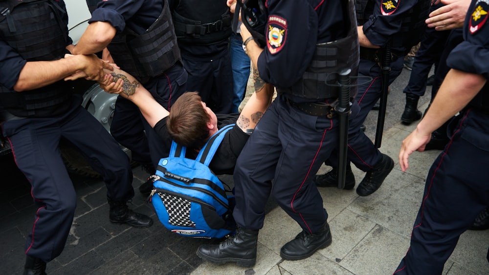 homme en veste noire et pantalon noir portant sac à dos bleu et noir