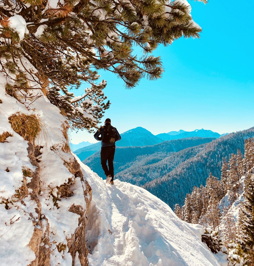person in black jacket and black pants standing on snow covered mountain during daytime
