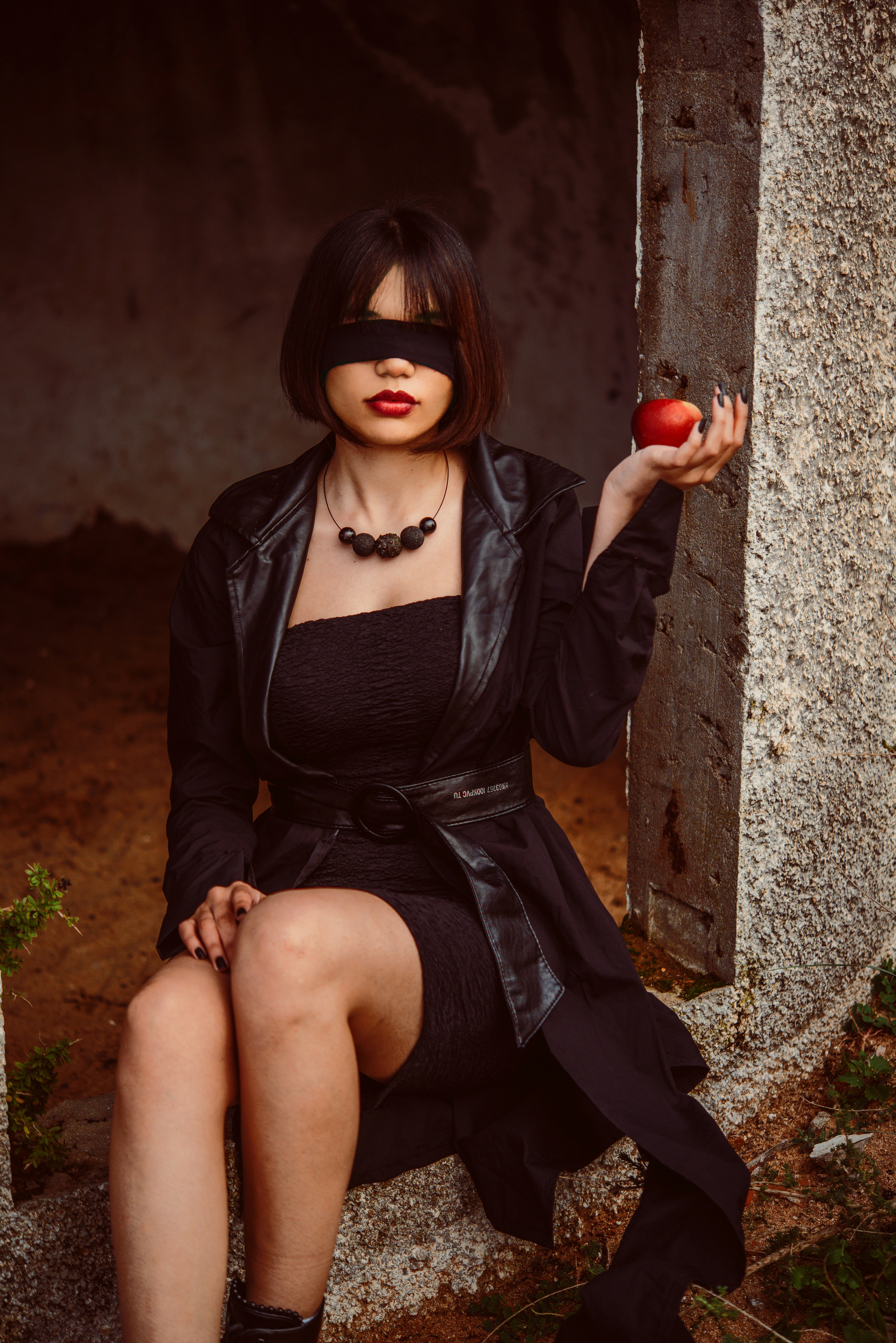 Wanita dengan jaket kulit hitam dan rok hitam duduk di dinding beton
