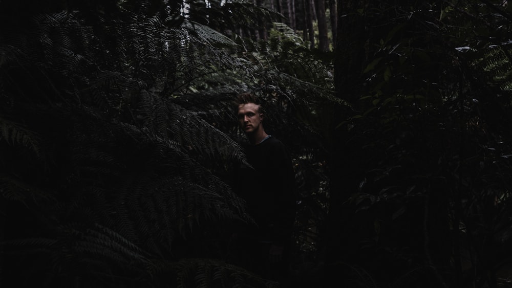 man in black long sleeve shirt standing beside green plant