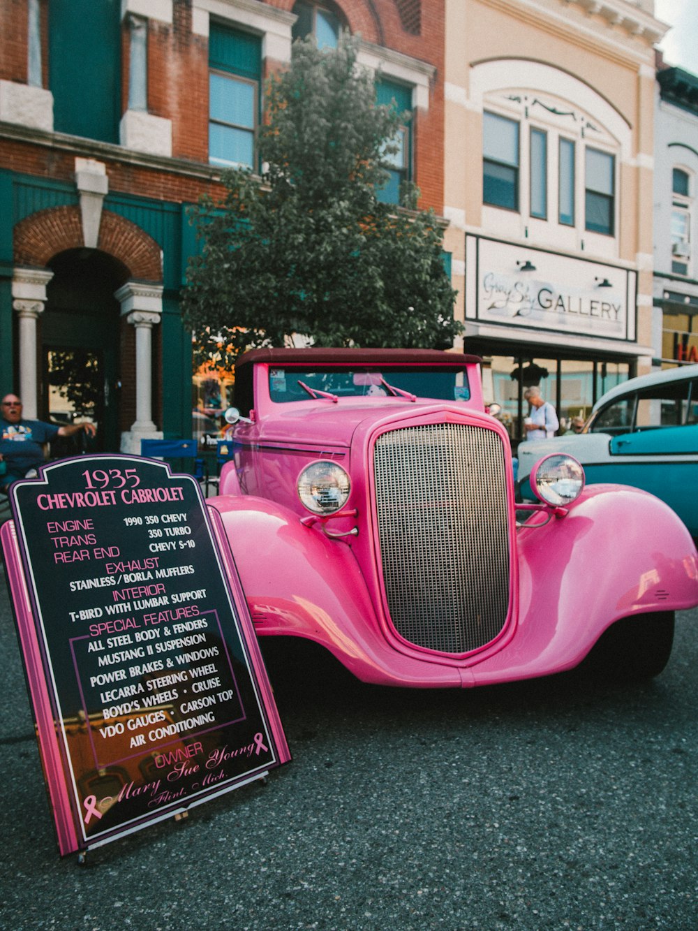 pink vintage car parked near green tree during daytime