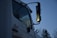 A close-up of a white truck featuring large side mirrors reflecting the evening light, with trees visible in the background. The name 'Joe' is written on the side of the door, and the word 'SERVICE' is partially visible below it.