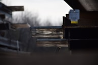 Several stacked steel beams with visible rust and a tag hanging from one. The background is blurred, creating depth and focus on the metal beams.