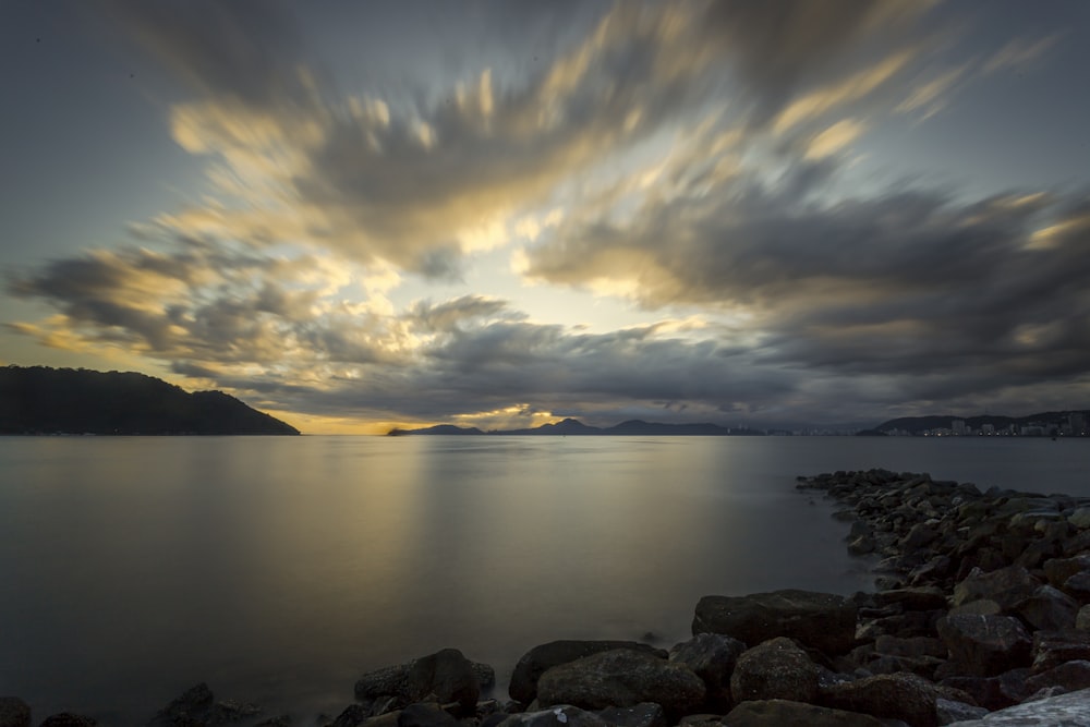 brown rocks near body of water under cloudy sky during daytime