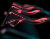 Curved metallic structures are highlighted by red and teal light against a black background, creating a futuristic and abstract appearance.