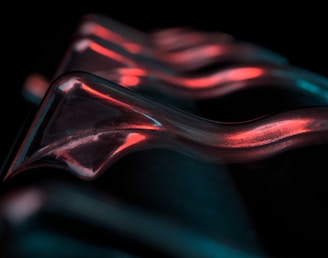 Curved metallic structures are highlighted by red and teal light against a black background, creating a futuristic and abstract appearance.