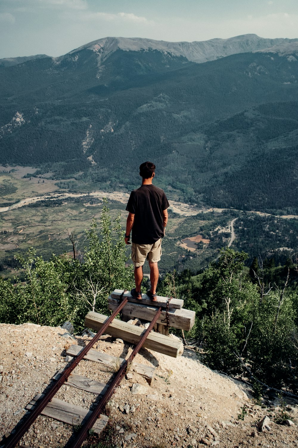 man in black t-shirt standing on brown wooden bench during daytime