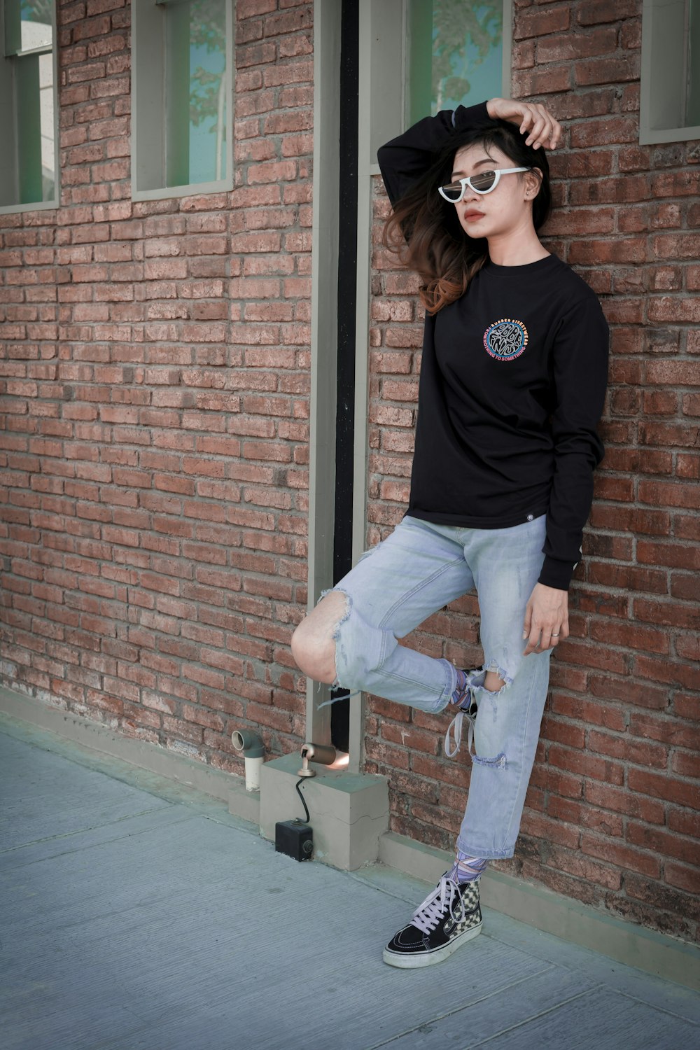 woman in black long sleeve shirt and gray denim jeans standing beside brown brick wall