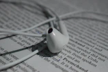 Close-up of earbuds tangled gently around a paperback with a floral cover.