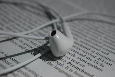 Close-up of earbuds tangled gently around a paperback with a floral cover.