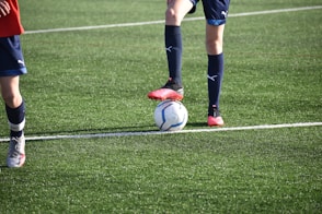 person in black and white soccer jersey kicking soccer ball on green grass field during daytime