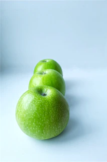 A trio of fresh green apples arranged neatly in a 3-column grid with soft natural lighting.
