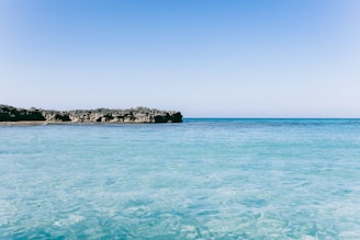 A peaceful coastal view of the Mediterranean Sea with clear blue water and a sunny sky.