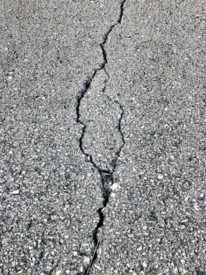 Before and after photos showing a cracked parking lot transformed into a clean, sealed surface.