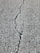 A close-up view of a cracked asphalt surface, showing a prominent crack running vertically through the rough, textured pavement.