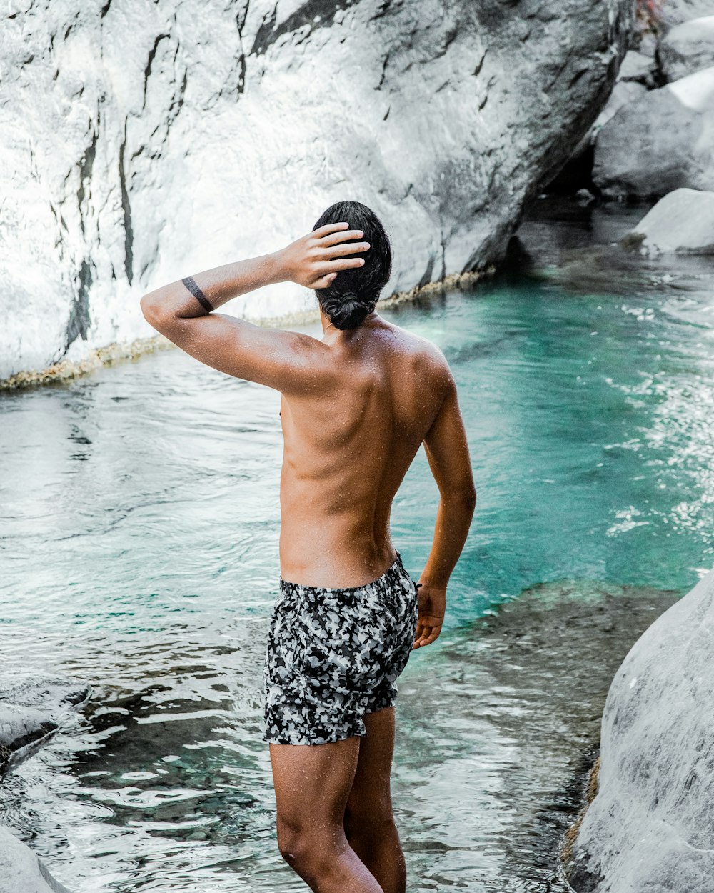 Mann in schwarz-weißen Shorts auf grauem Felsen vor Gewässer