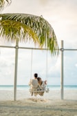 man in white shirt sitting on swing chair under coconut tree during daytime