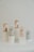 Five bottles of hair treatment products with labels displaying different fruit flavors are arranged on cylindrical white pedestals. The bottles are labeled 'hella co.' and include flavors such as grapefruit, kiwifruit, and blueberry.