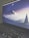 A laptop screen displays a serene digital artwork featuring a crescent moon above a snow-capped mountain surrounded by pine trees. The image is in shades of blue and purple, creating a calm, twilight atmosphere. The keyboard is visible in the foreground, conveying a workspace environment.