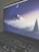A laptop screen displays a serene digital artwork featuring a crescent moon above a snow-capped mountain surrounded by pine trees. The image is in shades of blue and purple, creating a calm, twilight atmosphere. The keyboard is visible in the foreground, conveying a workspace environment.