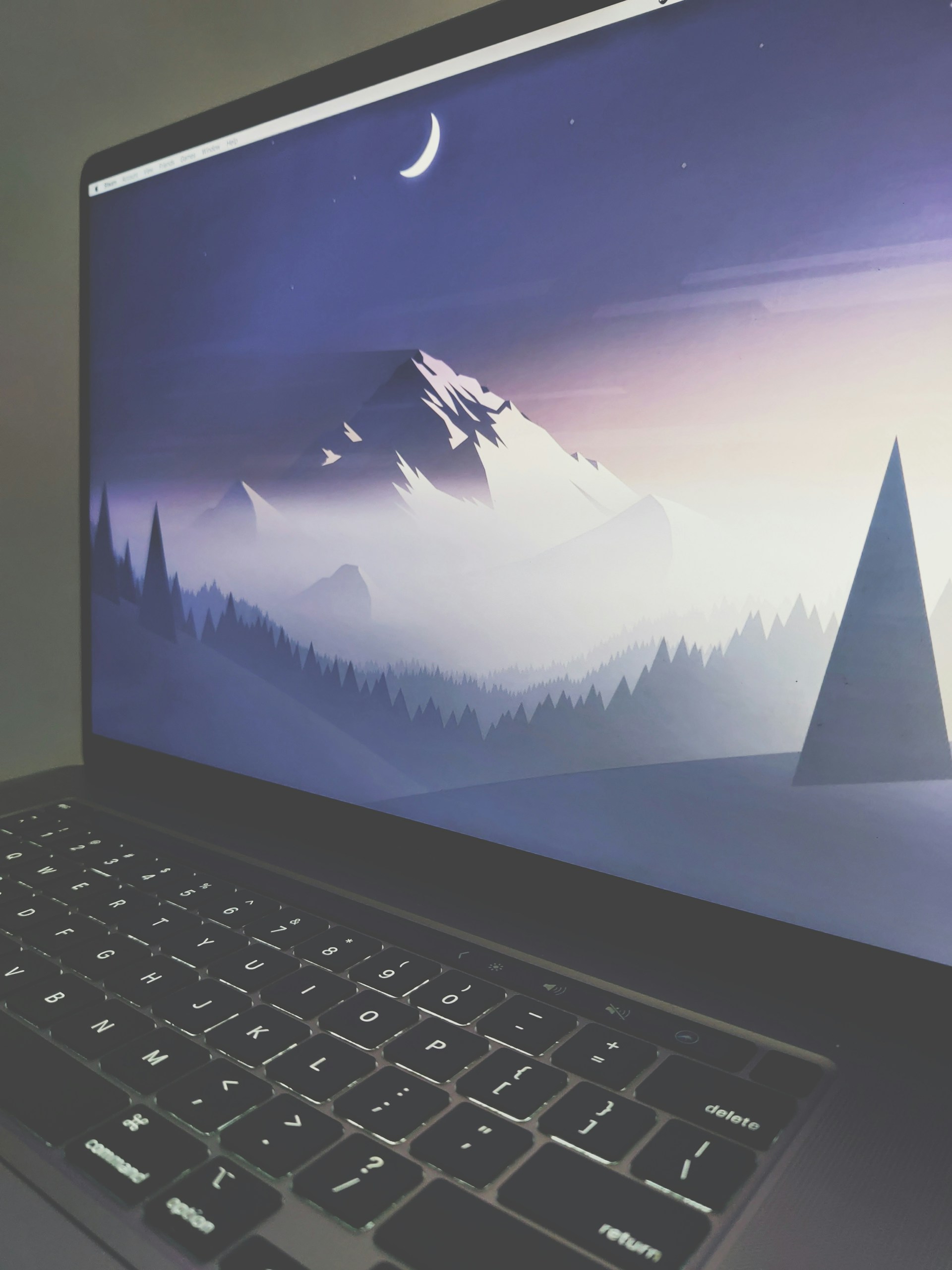 A laptop screen displays a serene digital artwork featuring a crescent moon above a snow-capped mountain surrounded by pine trees. The image is in shades of blue and purple, creating a calm, twilight atmosphere. The keyboard is visible in the foreground, conveying a workspace environment.