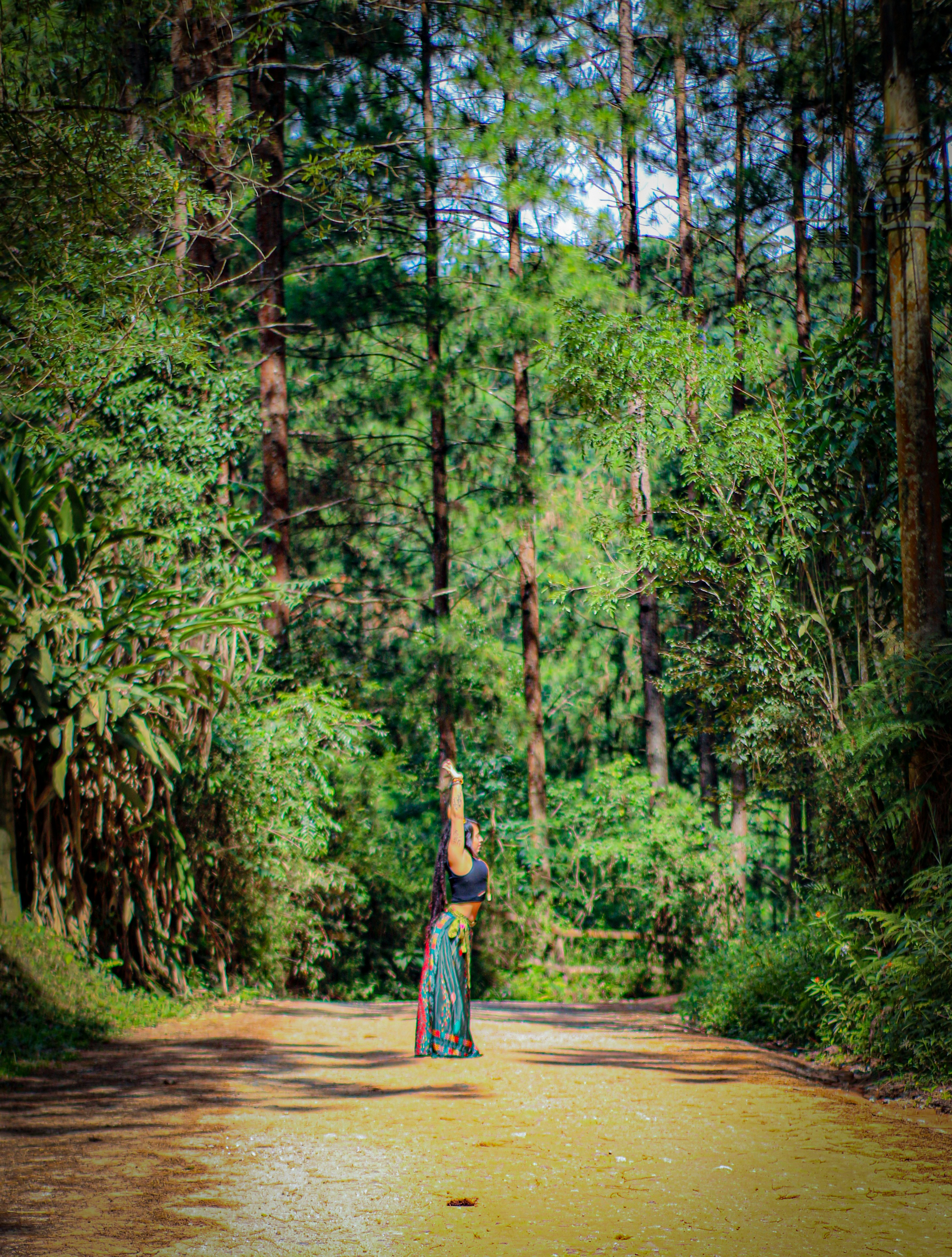 woman in blue and white dress walking on pathway surrounded by green trees during daytime