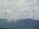 Three large wind turbines stand atop a hilly landscape, partially obscured by drifting clouds. The sky is overcast with dense cloud cover, creating a serene and slightly mysterious atmosphere. The turbines are spaced evenly across the ridge, symbolizing renewable energy and environmental stewardship.