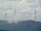 Three large wind turbines stand atop a hilly landscape, partially obscured by drifting clouds. The sky is overcast with dense cloud cover, creating a serene and slightly mysterious atmosphere. The turbines are spaced evenly across the ridge, symbolizing renewable energy and environmental stewardship.