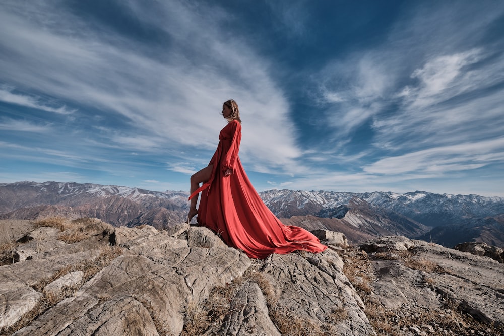 Frau in rotem Kleid sitzt tagsüber auf brauner Felsformation unter blauem Himmel