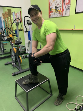 A friendly personal trainer in green athletic wear demonstrating a workout move in a gym.